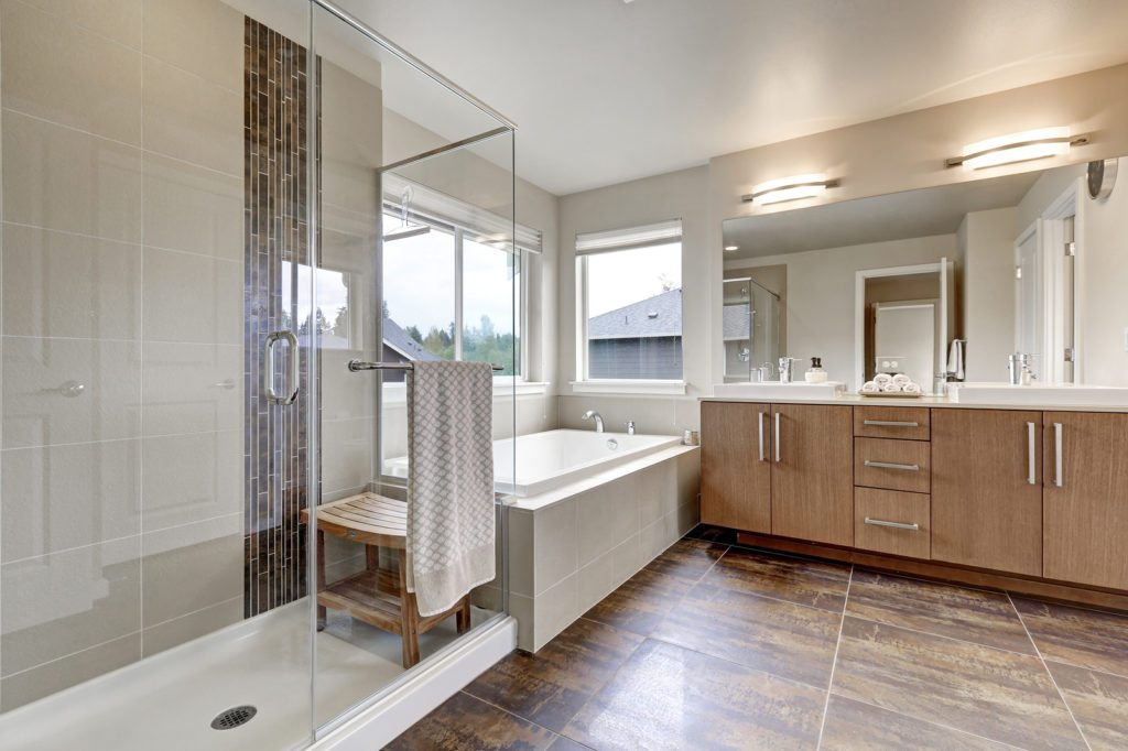 White modern bathroom interior in brand-new house. Double sink vanity with large mirror walk-in shower white bath tub and brown tile floor. Northwest USA